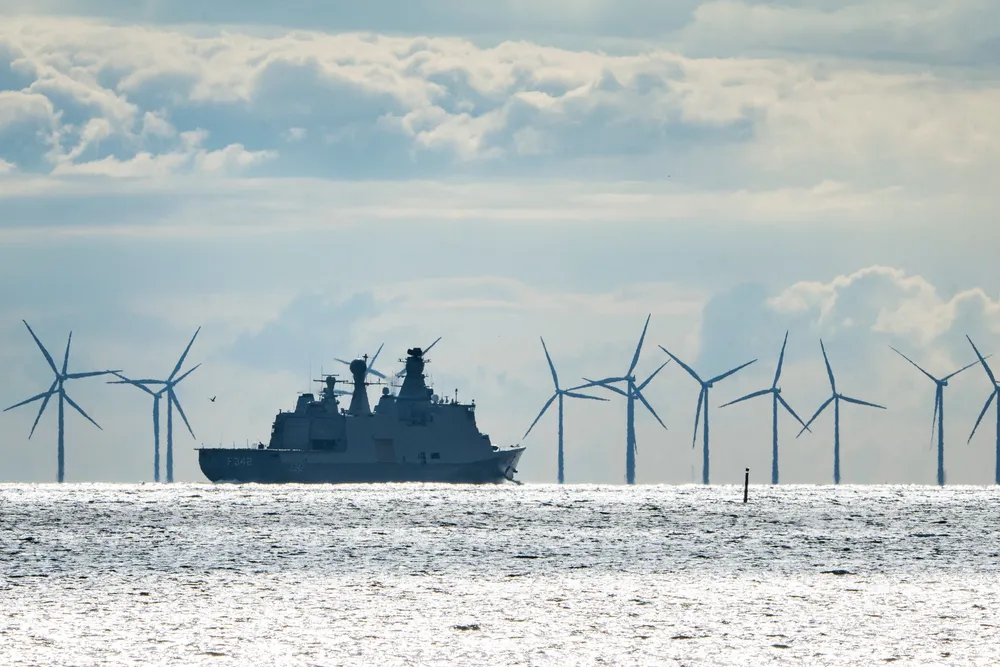 Danish frigate HDMS Esbern Snare patrols the water near wind turbines.